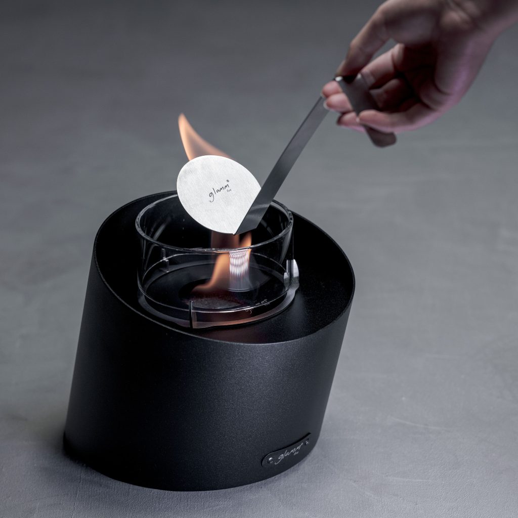 Person extinguishing the flame of the Contour tabletop bioethanol fireplace, demonstrating safety and ease of use.