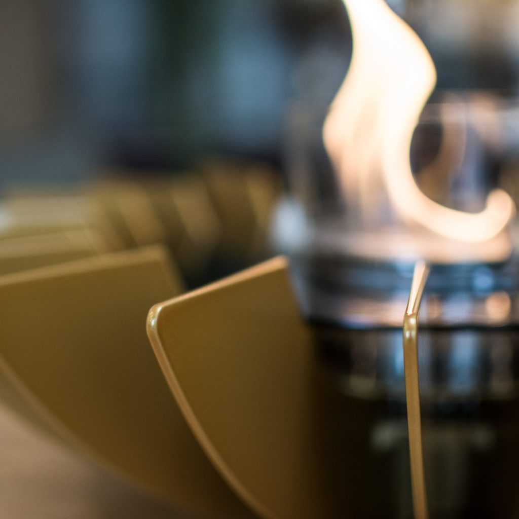 Close-up detail of the Cosmo bioethanol tabletop fireplace by GlammFire in gold, showing the intricate petal design and the central flame in a glass container.