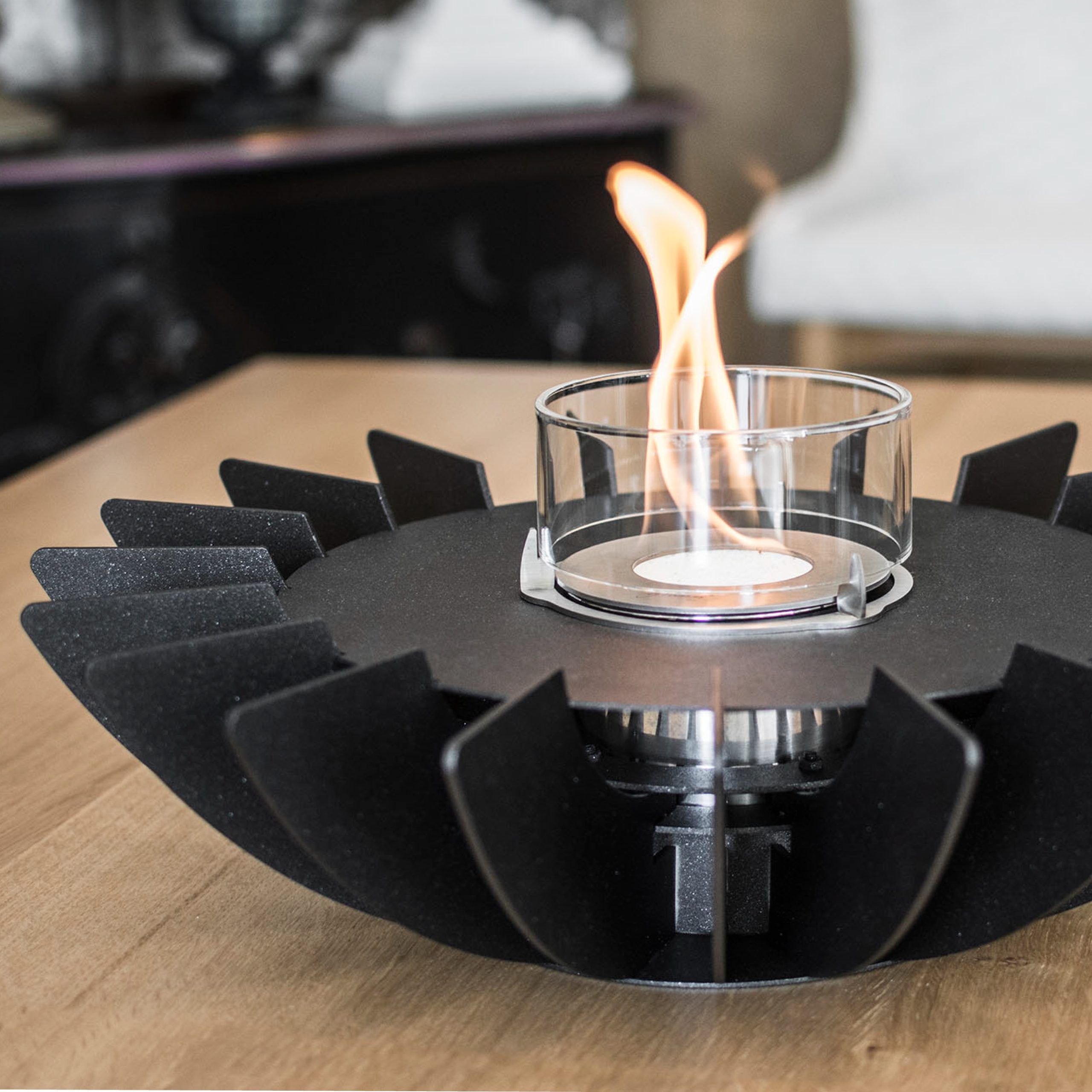 Close-up detail of the Cosmo bioethanol tabletop fireplace by GlammFire in black, showcasing the sleek petal design and the central flame in a glass container.
