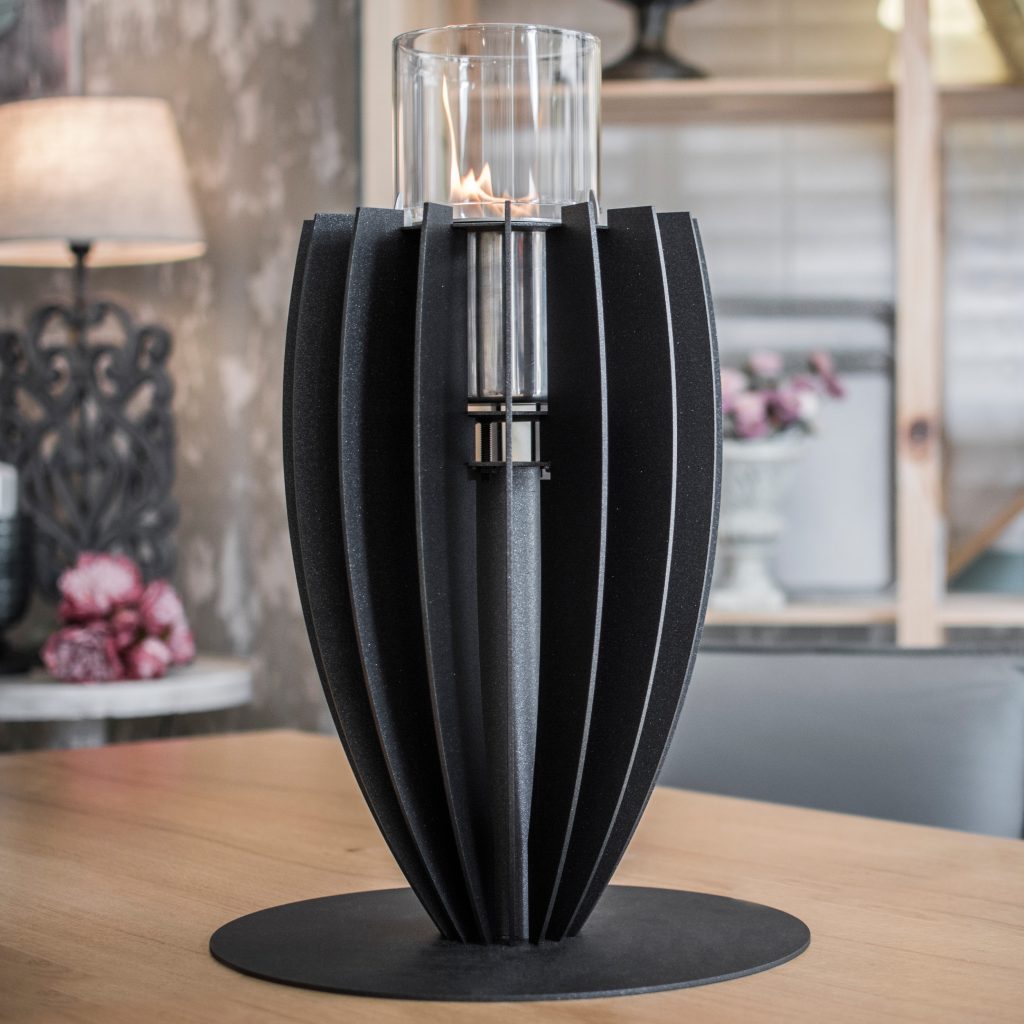 Tuli bioethanol tabletop fireplace by GlammFire in black, placed on a table, showcasing its elegant vertical design with a central flame in a glass container