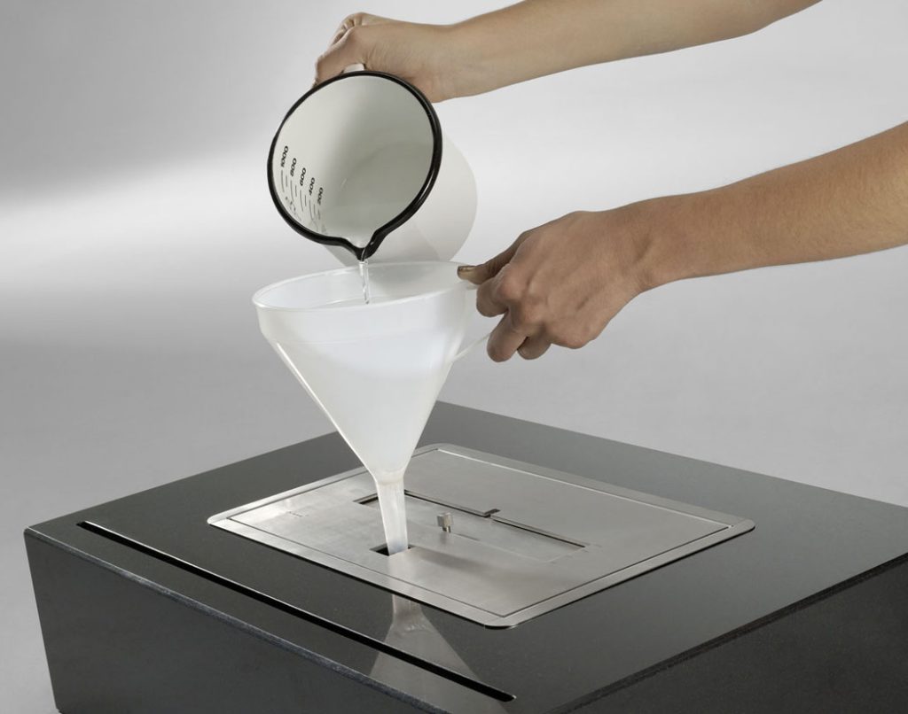 Filling the fuel tank of the Burner II bioethanol fireplace, demonstrating easy operation and maintenance.
