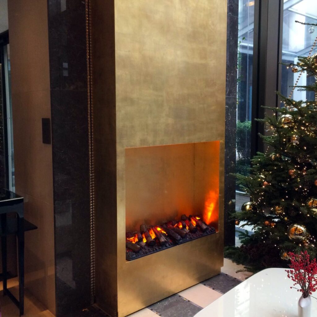 GlammFire Kit Glamm 3D Plus 1000 electric fireplace with realistic flame effect, built into a gold-finish wall in a modern Turkish interior beside a decorated Christmas tree