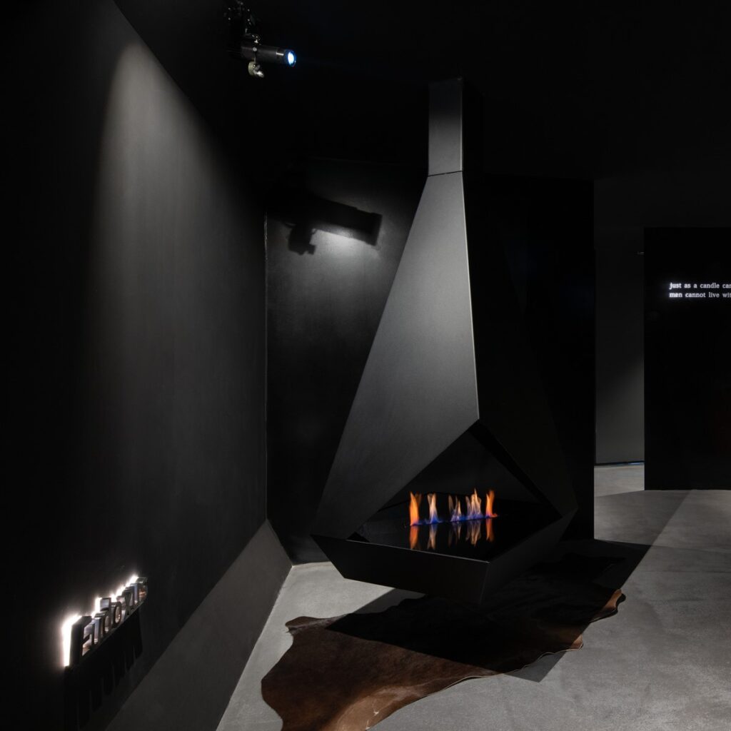Lareira suspensa Eudoxus a bioetanol da GlammFire em showroom contemporâneo com design geométrico preto.