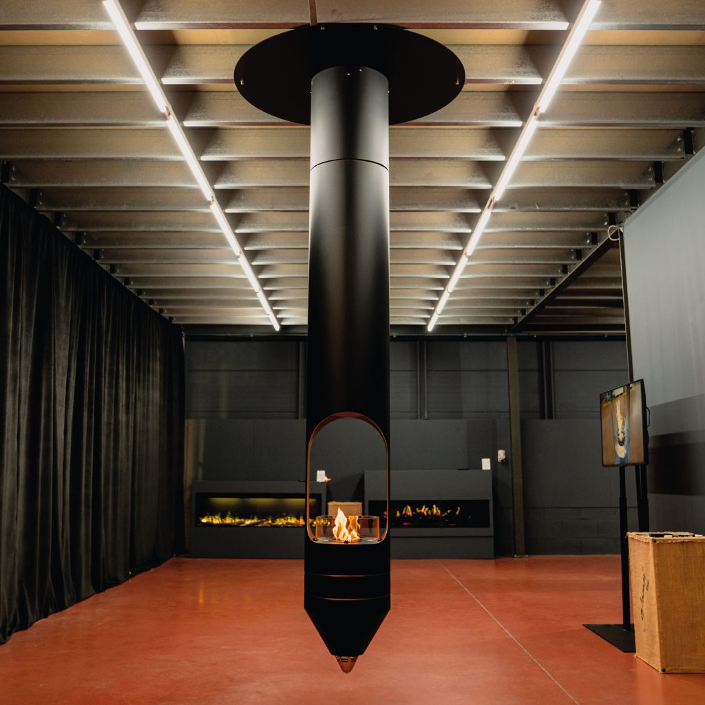Signature suspended bioethanol fireplace in a modern industrial setting with sleek black design and warm flame.