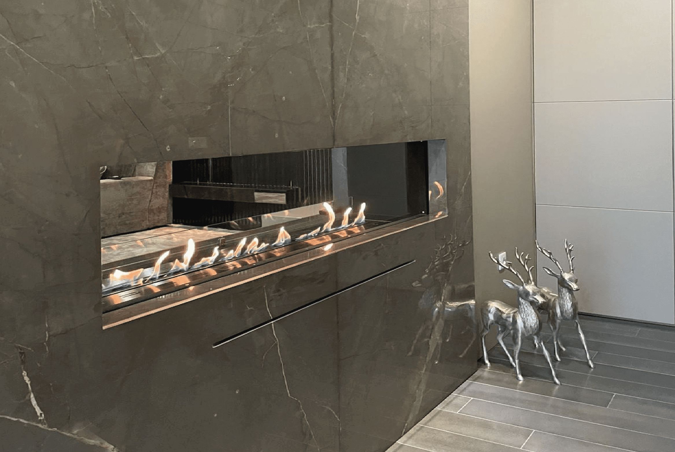 GlammBox EVOPlus bioethanol fireplace integrated in a luxury marble-clad living room with metallic deer sculptures.