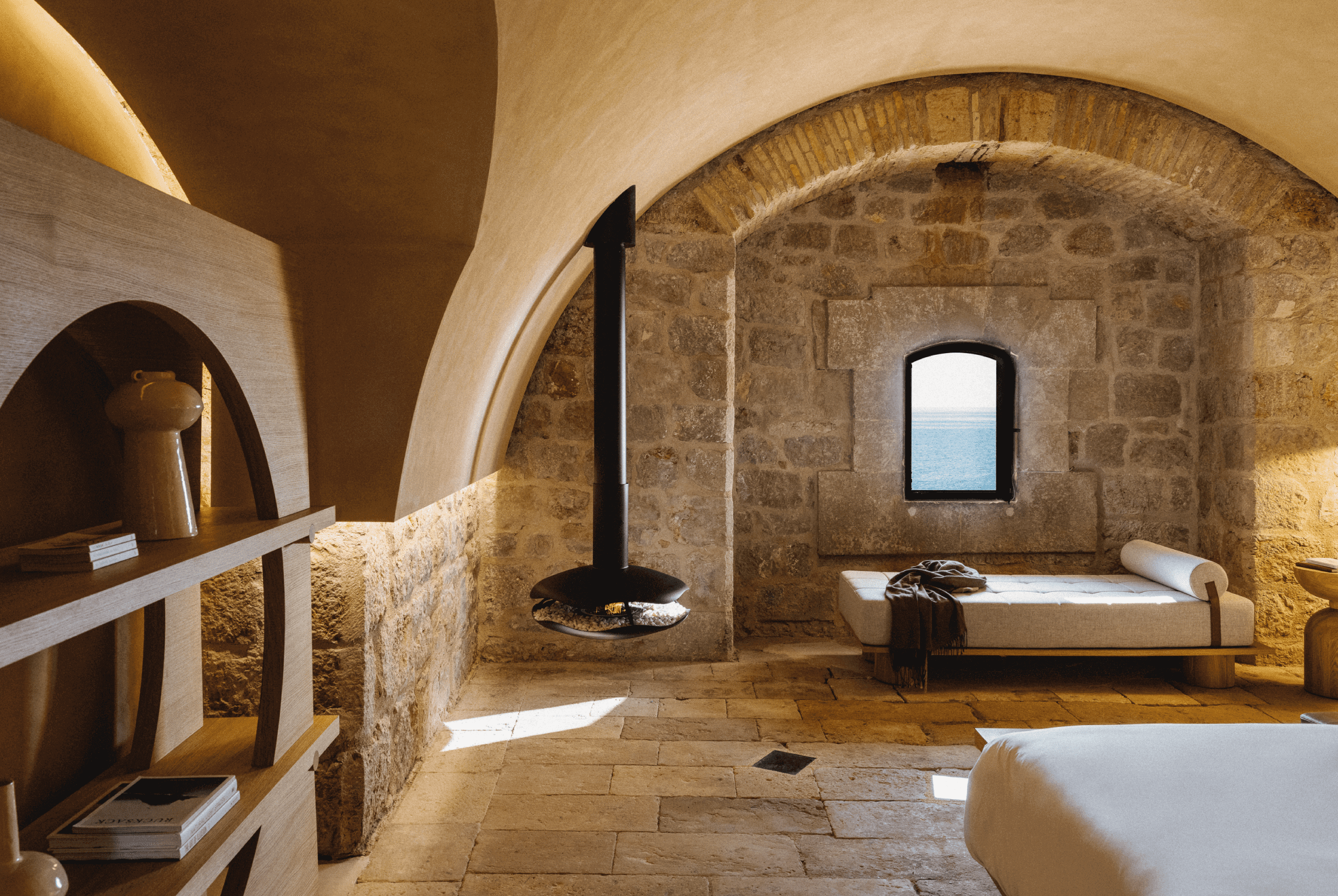 Perola suspended bioethanol fireplace by GlammFire in a rustic stone room with vaulted ceilings and sea view"