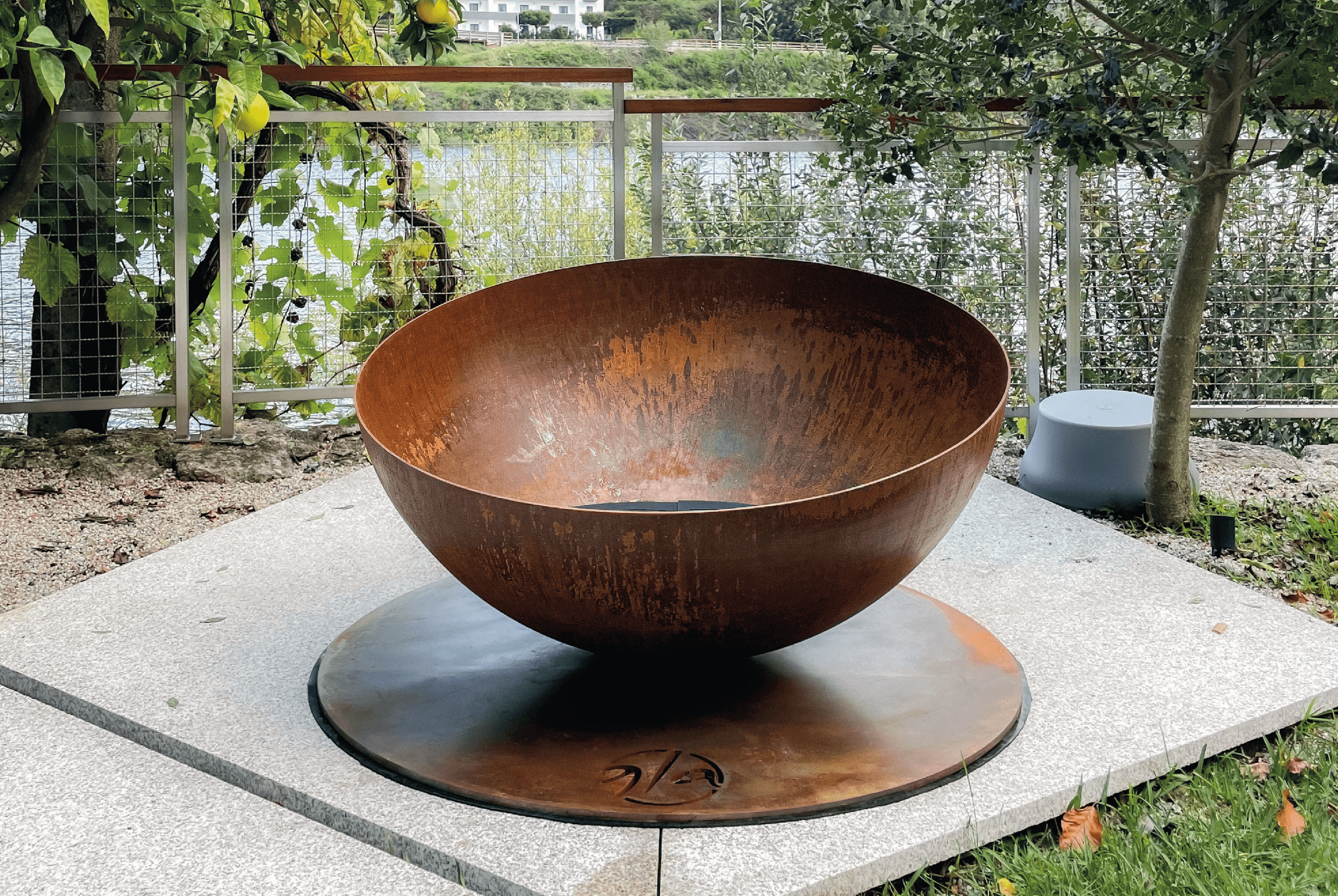 Solace fire pit by GlammFire in a rustic outdoor setting with a corten steel finish