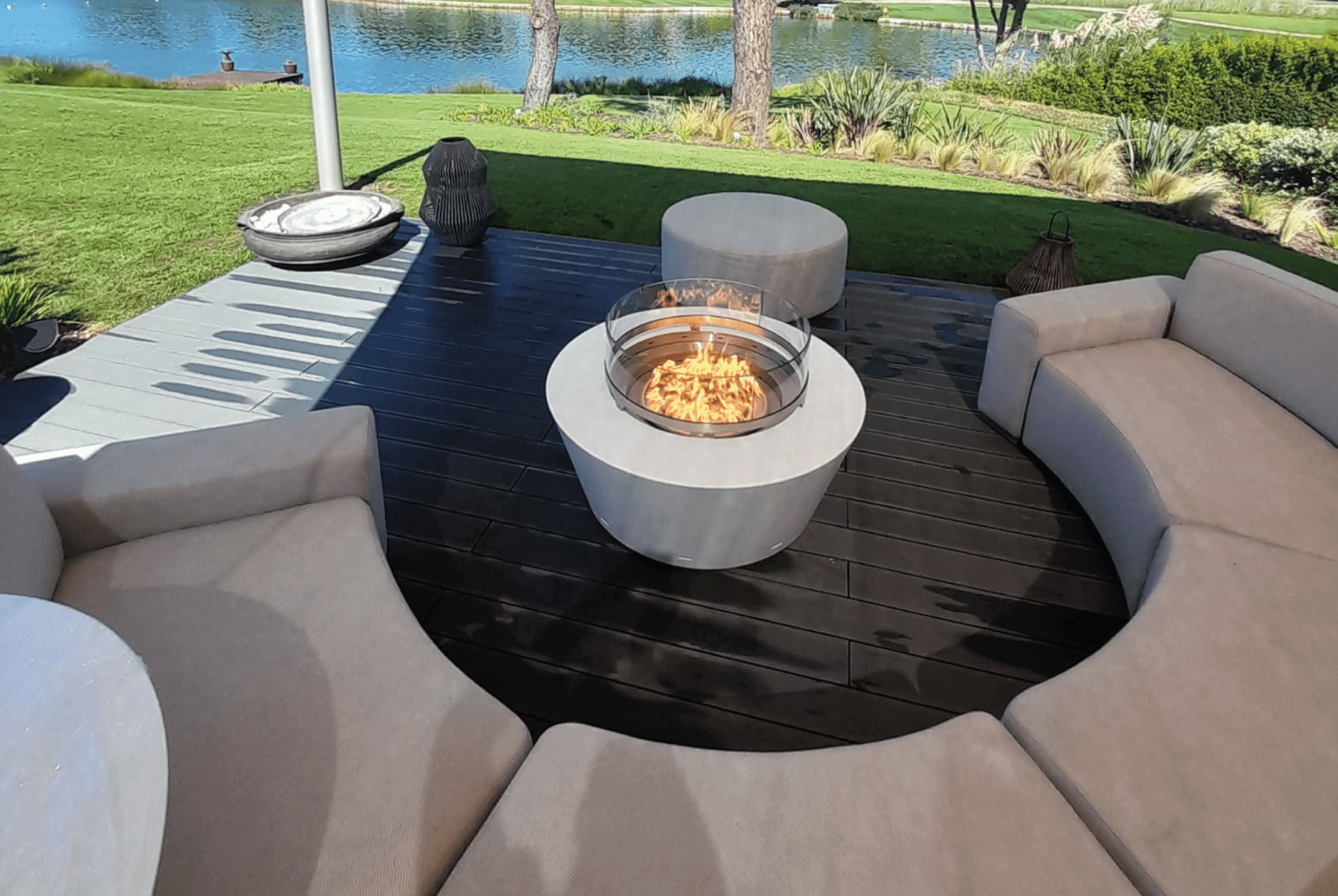 Gas fire pit in a modern outdoor seating area with a view of a lake and greenery