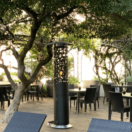 Tile Hyperion gas patio heater by GlammFire in an elegant outdoor hospitality setting surrounded by trees