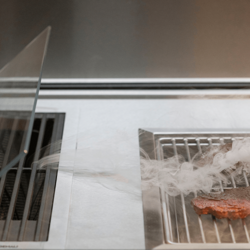 Close-up of Fortezza outdoor kitchen with grilled food, smoke flow and stainless steel cooking system