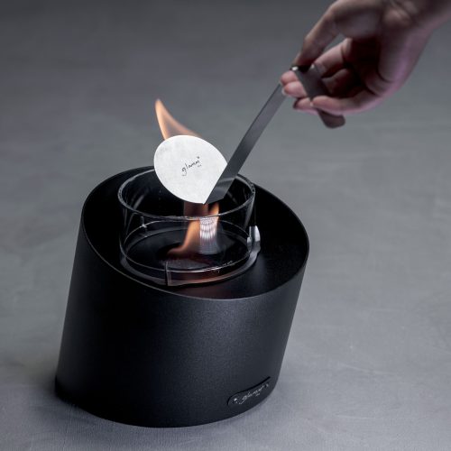 Person extinguishing the flame of the Contour tabletop bioethanol fireplace, demonstrating safety and ease of use.