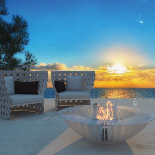 Lareira Cosmo 13 branca a bioetanol da GlammFire em terraço exterior com vista para o mar ao pôr do sol.