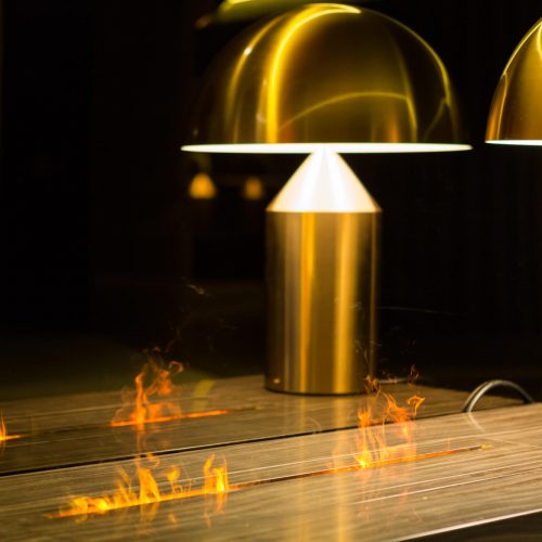 lose-up of GlammFire Gema fireplace flames reflected on a wooden surface beside modern golden dome lamps in a contemporary interior setting
