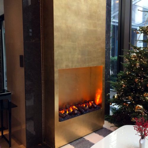 GlammFire Kit Glamm 3D Plus 1000 electric fireplace with realistic flame effect, built into a gold-finish wall in a modern Turkish interior beside a decorated Christmas tree