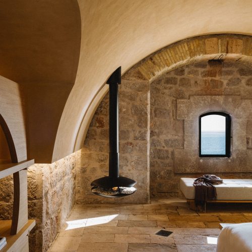 Perola suspended bioethanol fireplace by GlammFire in a rustic stone room with arched ceilings and sea view