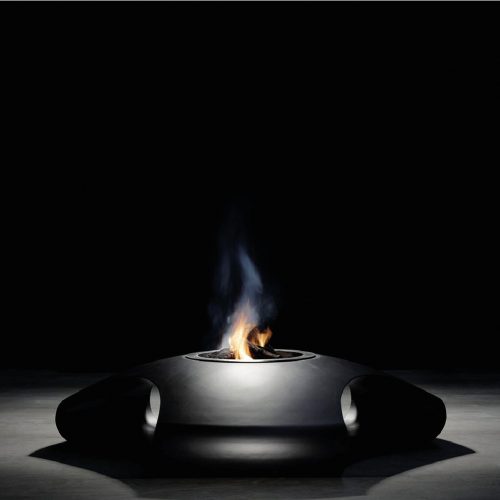 Vaudeville fire pit in a minimalistic dark setting with a person sitting nearby.