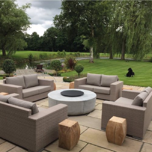 Luxurious outdoor seating area featuring the Zarzuela Fire Pit by GlammFire, a modern round concrete fire pit set in a serene garden with lush green surroundings.