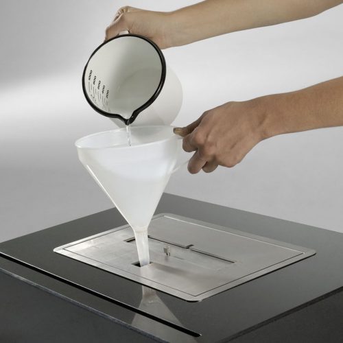 Filling the fuel tank of the Burner II bioethanol fireplace, demonstrating easy operation and maintenance.